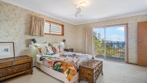 Un dormitorio con cama, cómoda, mesita de noche, ventilador de techo y balcón con vistas.