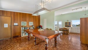A dining area with a wooden table and chairs, a bookshelf, and a view through a door.
