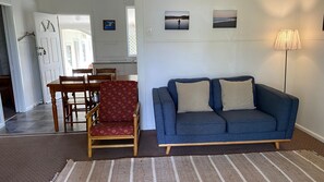 A living room with a blue sofa, a wooden chair, a dining table, and a lamp.