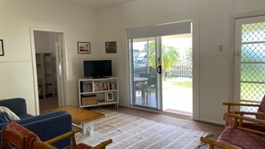 A living room with a sofa, a television, a bookshelf, and a sliding glass door leading to an outdoor area.