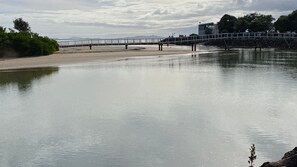 A calm river with a bridge, a sandy beach, and a building in the background.