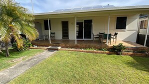 A house with a covered patio, a lawn, and a palm tree. - Fleur Cottage, 7 Willow Street (Crescent Head)