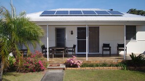 A house with a covered porch, solar panels on the roof, and a small garden with pink flowers.