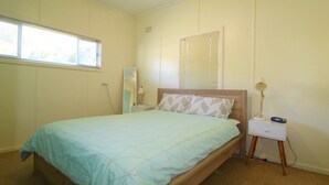 Een slaapkamer met een enkel bed, een nachtkastje met een lamp en een raam met zonwering.