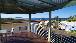A covered outdoor area with a view of a coastal town, a wooden deck, and a chair.