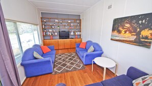 Een woonkamer met twee blauwe banken, een witte salontafel, een boekenkast en een schilderij van een zonsondergang.