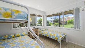 A room with bunk beds, a desk, and large windows offering a view of the outside.