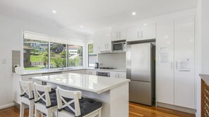 Cozinha moderna com armários brancos, geladeira de aço inoxidável, micro-ondas e uma grande janela com vista para uma área residencial.