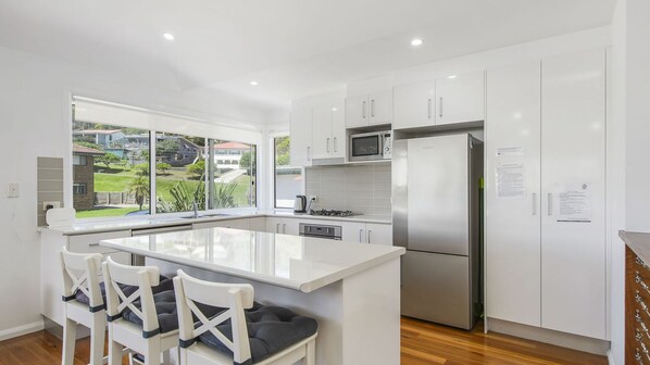 A modern kitchen with white cabinetry, a stainless steel refrigerator, a microwave, and a large window overlooking a residential area.