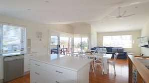 A spacious living area with a dining table, white furniture, and a balcony with a view.