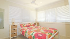A bedroom with a bed, two bedside tables, a ceiling fan, and a window with blinds.