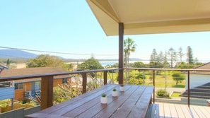 A wooden deck with a table and potted plants, overlooking a residential area and a body of water.