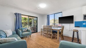 A modern living room with a sofa, dining table, chairs, and a TV.