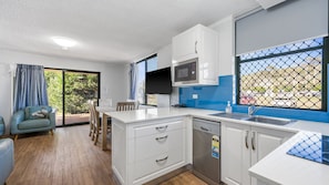 A compact kitchen with white cabinets, a microwave, and a sink. There is a dining area with a table and chairs, and a large window with a view of the outside.