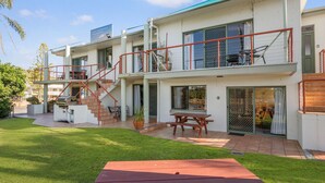 Un edificio residencial de dos pisos con un espacio exterior cubierto, una escalera y un patio con mesa y sillas.