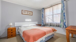 Un dormitorio con cama, mesita de noche, lámpara y ventana con cortinas.