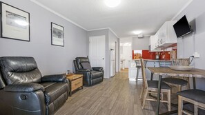 A modern living room with leather sofas, a dining table with chairs, and a kitchen area with a TV mounted on the wall.