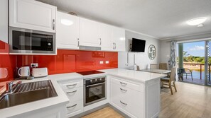 A modern kitchen with white cabinets, a red backsplash, stainless steel appliances, and a dining area with a view.