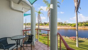 Un balcón con mesa y sillas, con vista a un lago con palmeras y una zona verde.