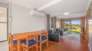 A room with a wooden dining table, chairs, a sofa, and a sliding glass door leading to an outdoor area.