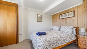 Un dormitorio con cama, un armario de madera, una mesita de noche con lámpara y un espejo en la pared.