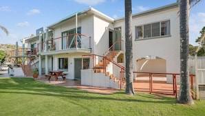 Una casa de dos pisos con un patio, mobiliario exterior y una escalera.