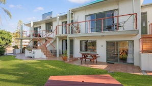Un edificio residencial de dos pisos con un espacio exterior cubierto, una escalera y un patio con mesa y sillas.