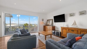 A modern living room with a large sliding glass door leading to a balcony, a flat-screen TV mounted on the wall, and a wooden cabinet with decorative items.