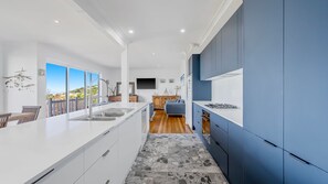 A modern kitchen with a large island, a dining area with a view, and a living space with a sofa and TV.