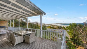 A covered outdoor deck with a table and chairs, overlooking a beach and ocean. - Beau Soleil, 28 East Street (Crescent Head)