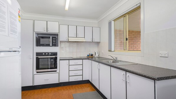 A compact kitchen with white cabinets, a built-in oven, a microwave, and a sink.