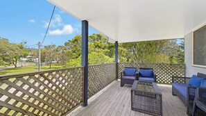A covered outdoor deck with wooden flooring, a lattice fence, and two wicker chairs with cushions.