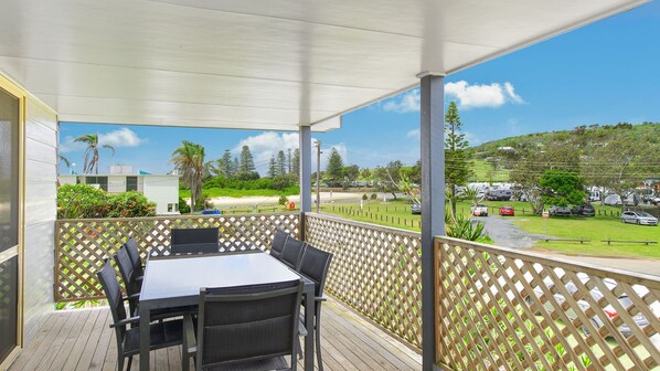A covered outdoor area with a table and chairs, overlooking a parking lot and a hilly landscape. - Bellhaven 1, 17 Willow Street (Crescent Head)
