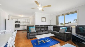 A modern living room with a sectional sofa, a flat-screen TV, and a dining area with white furniture.