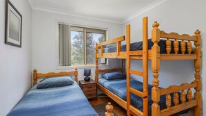 A bedroom with bunk beds, a bedside table, a lamp, and a window with a view of trees.