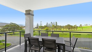 Une terrasse extérieure avec une table et des chaises, un pilier en béton et une vue sur un paysage verdoyant, avec des arbres et une colline.