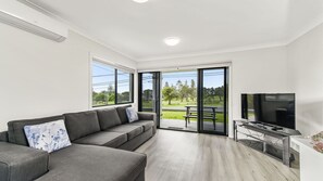 A modern living room with a grey sofa, a flat-screen TV, and a sliding glass door leading to an outdoor patio.