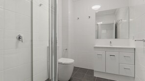 A modern bathroom with white tiles, a glass shower enclosure, a toilet, and a vanity with a mirror.