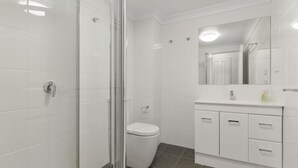 Une salle de bain moderne avec une douche à parois de verre, des toilettes blanches et un meuble-lavabo avec un miroir.