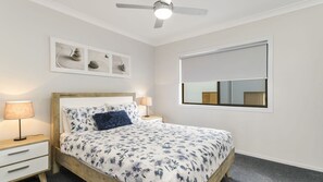 A bedroom with a bed, bedside lamps, a ceiling fan, a window, and a wall-mounted artwork.
