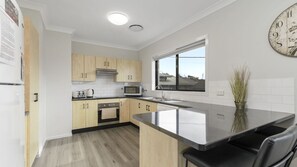 A modern kitchen with light wood cabinets, a stainless steel countertop, a built-in oven, and a window providing a view.
