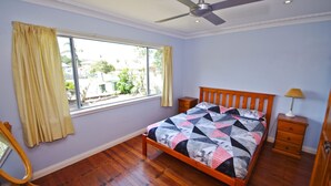 Un dormitorio con una cama, mesitas de noche de madera, un ventilador de techo y una ventana con cortinas.