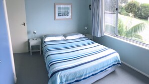 A bedroom with a bed, a nightstand, a lamp, a framed picture on the wall, and a window with a view of greenery. - Clareview, 8 Korogora Street (Crescent Head)