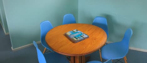 A round wooden table with a magazine, surrounded by four blue chairs in a room with light green walls.