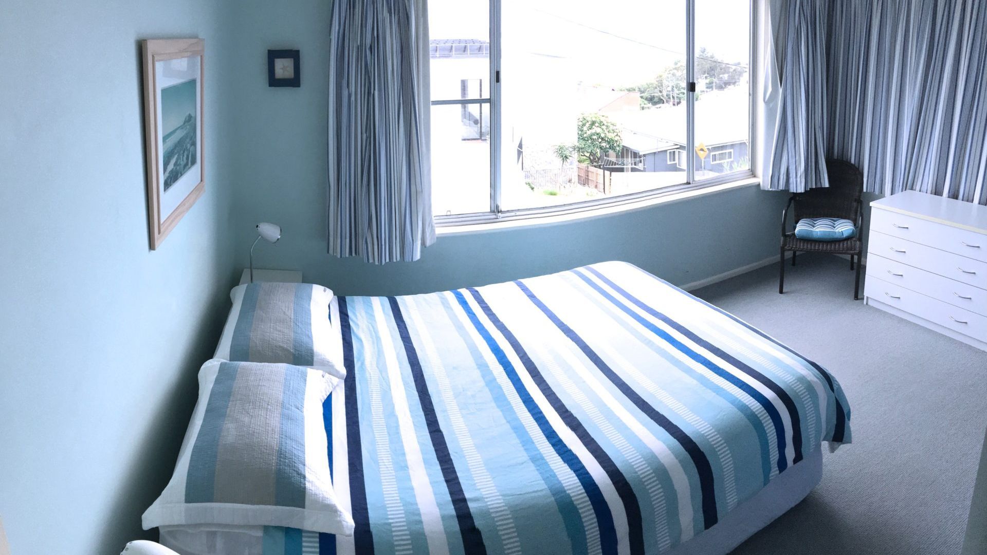 Un dormitorio con cama, una silla, cómoda y ventana con cortinas.
