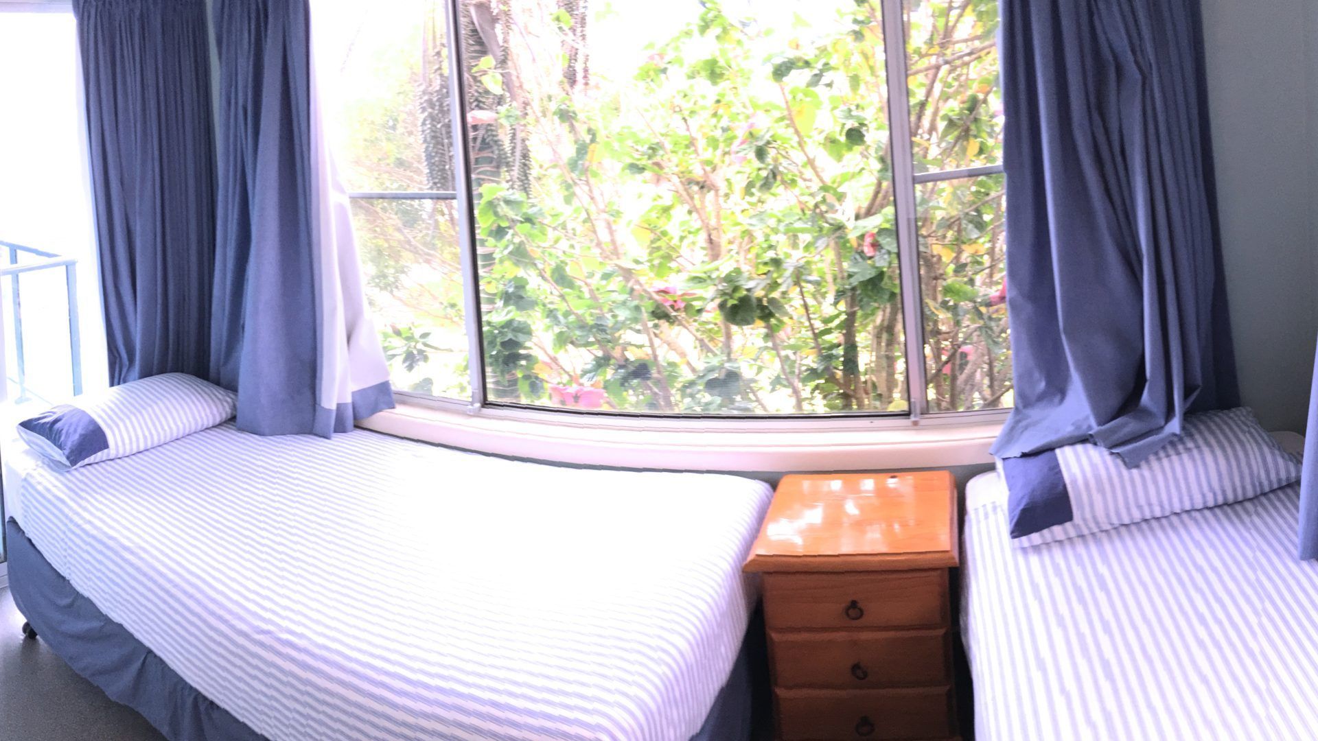 A bedroom with a large window, two beds, and a wooden dresser.