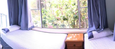 A bedroom with a large window, two beds, and a wooden dresser.
