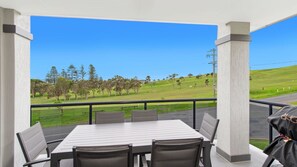 Un espace extérieur abrité, aménagé avec une table et des chaises, offrant une vue sur un paysage verdoyant, parsemé d’arbres et surplombé d’un ciel bleu dégagé.