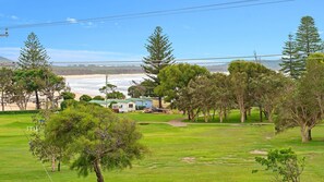 A coastal property with a grassy lawn, trees, a beach, and a small house with a trailer.