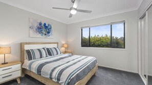 Une chambre à coucher avec un lit, un ventilateur de plafond, une fenêtre donnant sur un paysage verdoyant et un tableau accroché au mur.